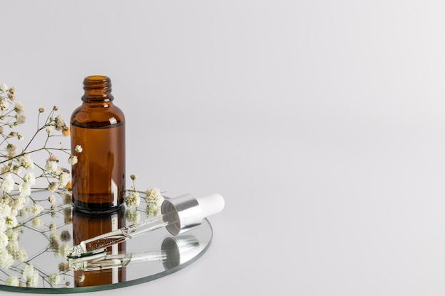 An open bottle with a moisturizer and skin nourishing agent stands on a round mirror with a filled pipette a copy of the space selective focus