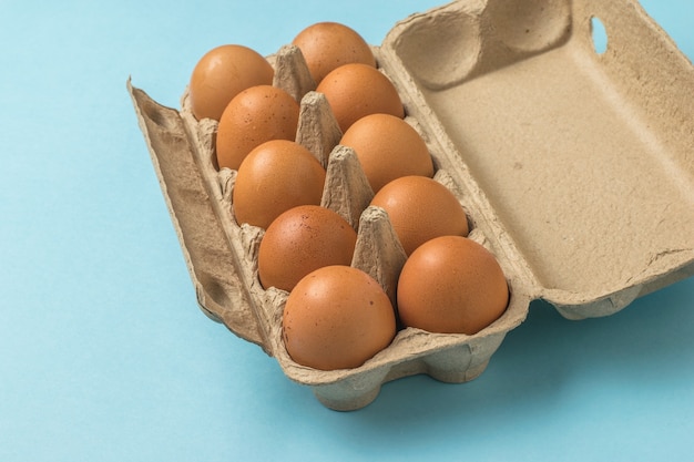 An open box of brown eggs on a blue surface. A natural product.