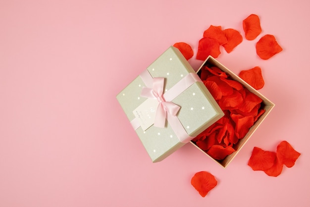 Open box filled with rose leaves on pink background