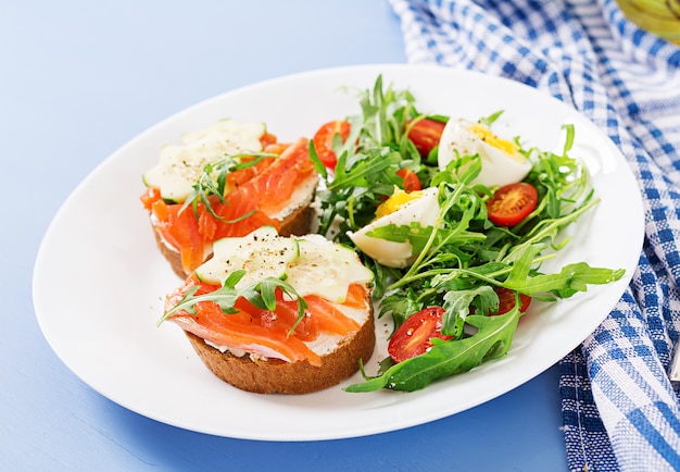 Open broodjes met zalm, roomkaas en roggebrood in een witte plaat en een salade