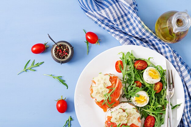 Open broodjes met zalm, roomkaas en roggebrood in een witte plaat en een salade