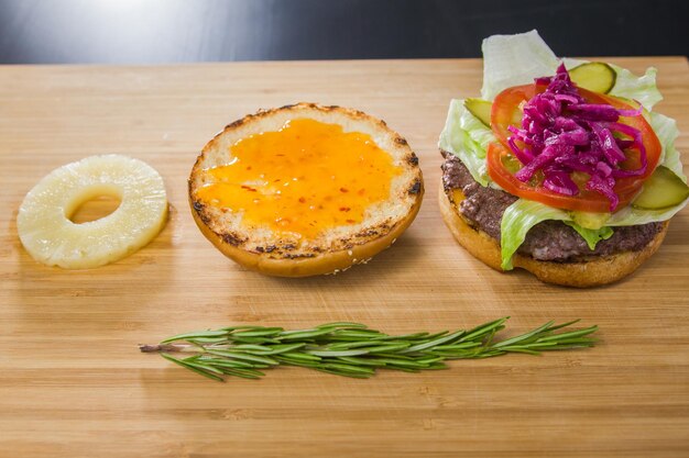 Open burger with pineapple and red onion on wooden board, top view