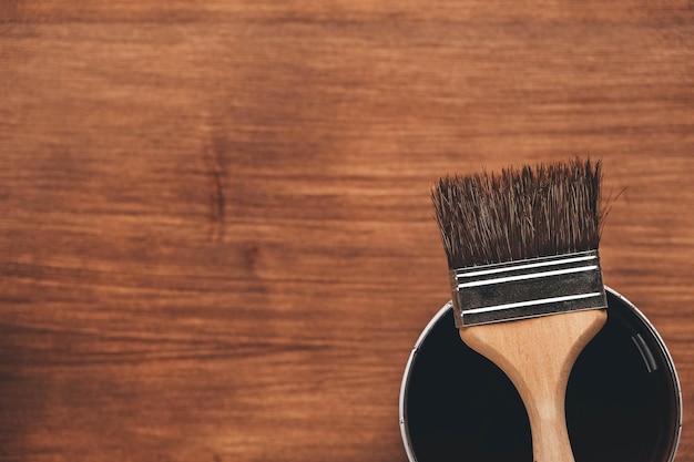 Open can of paint with brown brush on it on wooden background