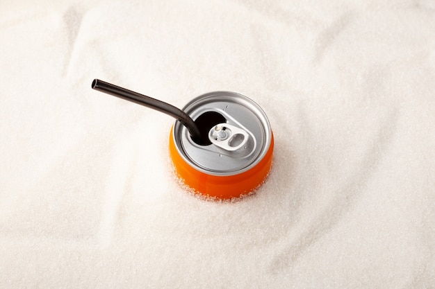 An open can of sweet carbonated drink with a drinking straw into a pile of granulated sugar