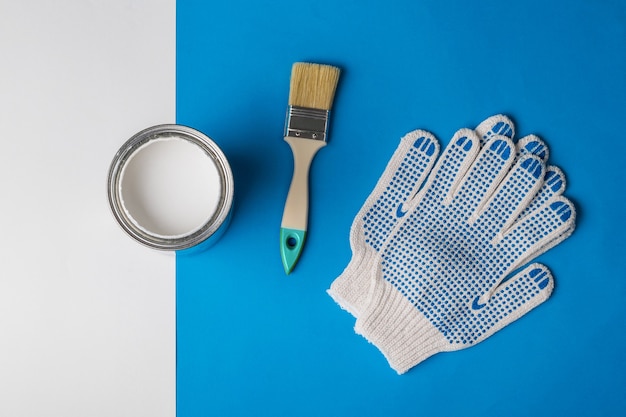 An open can of white paint, gloves and a brush on a blue and white