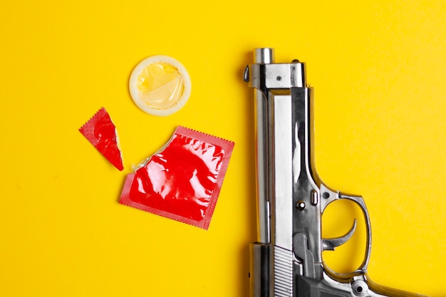 Open condoom ligt op een gele achtergrond in de buurt van de snuit van een pistool, het concept van veilige seks