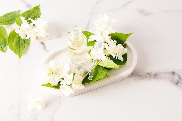 Open cosmetic bottle with an organic natural product based on\
jasmine oil on a white plaster tray with flowers alternative to\
medicine