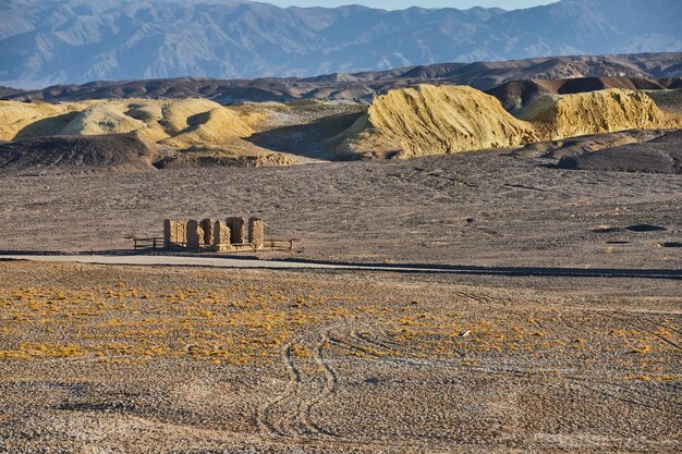Open desert landscape with tire marks and old stone structure by mountains