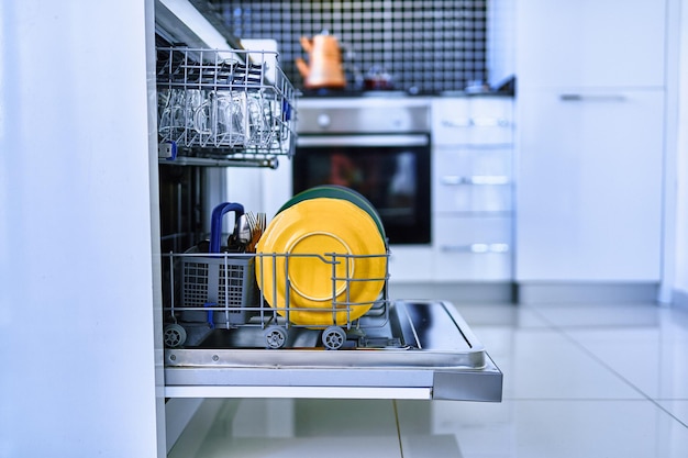 Open dishwasher with shiny clean dishes in a white home kitchen