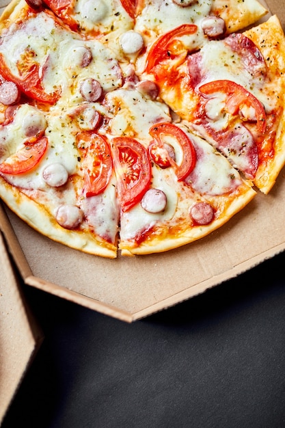 Open doos met hete smakelijke Italiaanse gesneden pizza op zwarte achtergrond, heerlijk fastfood, levering concept