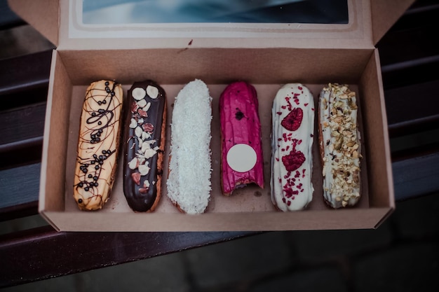 Open doos met veel kleurrijke traditionele Franse dessert-eclairs en een hapje op de bank Cadeauconcept