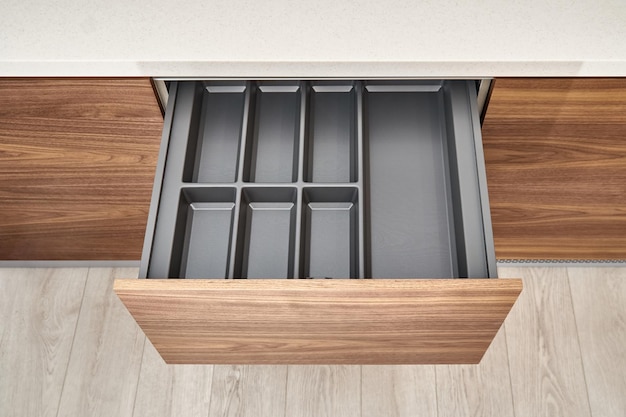 Open drawers with cutlery tray in kitchen of walnut wood with acrylic solid surface countertop