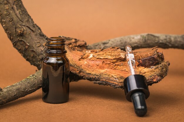 An open dropper bottle and an old tree on a brown background. Cosmetics and medicinal products based on natural minerals.