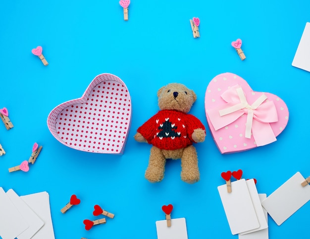 Open empty cardboard box in the form of a heart and little brown teddy bear on a light blue 