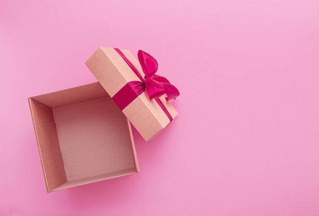 Open empty gift box with satin ribbon bow on pink background