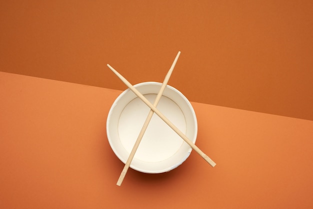 Open empty noodle bowl and pair of wooden sticks on brown background, top view