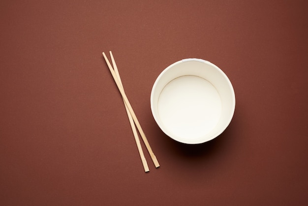 Open empty noodle bowl and pair of wooden sticks on brown background