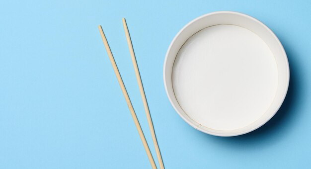 Open empty noodle bowl with and pair of wooden sticks on blue background top view