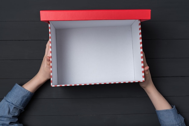 Open empty red box in children's hands on black . Top view.