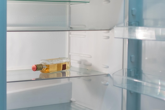 Open empty refrigerator with a bottle of alcohol