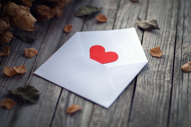 Open envelope with red paper heart among dry roses petals