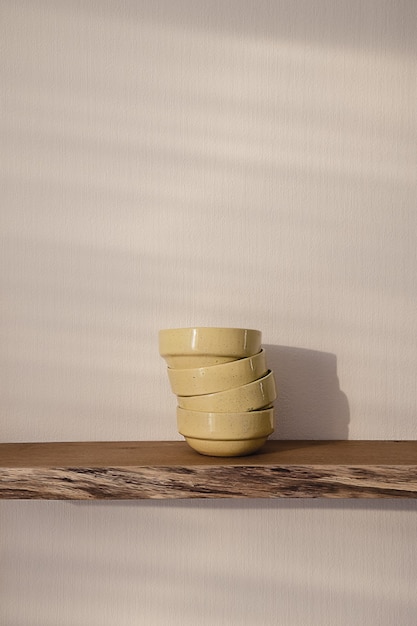 Open floating wooden shelf with a pile of four yellow handmade ceramic plates hanging on a white wallin a modern design living room. cozy minimalist home concept.