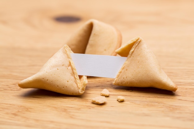 Photo a open fortune cookie with crumbs and note on wooden table background. taken in studio with  a 5d mark iii.
