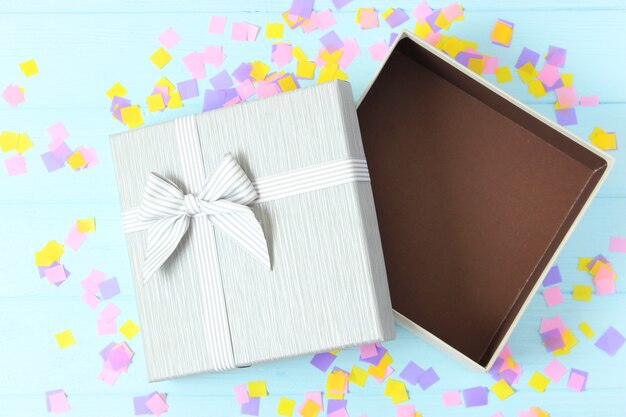 Open gift box and confetti on a colored background top view