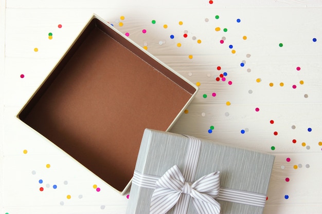 Open gift box and confetti on a colored background top view