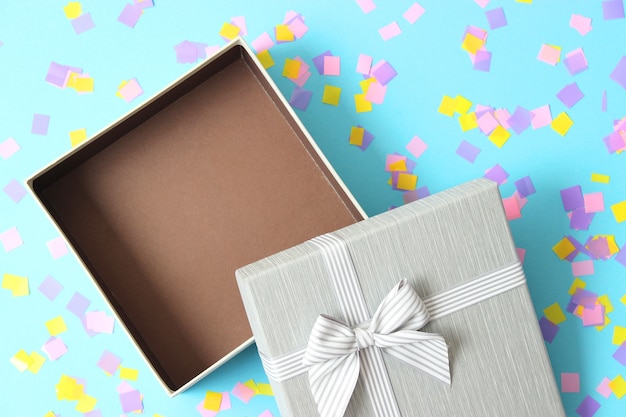 Open gift box and confetti on a colored background top view