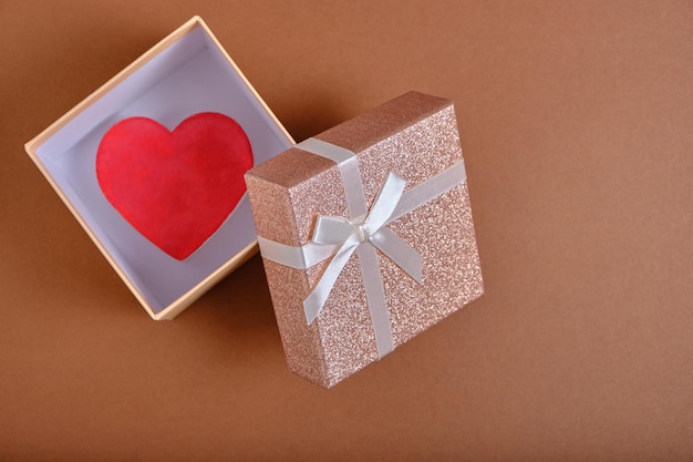 La confezione regalo aperta con cuore all'interno di sfondo marrone è legata con un nastro beige con fiocco