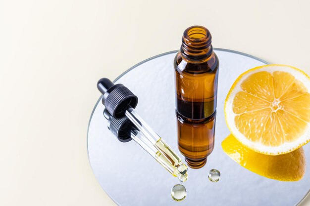 Photo an open glass bottle stands on a mirror with a slice of juicy lemon and a pipette filled with a natural cosmetic a serum based on lemon oil