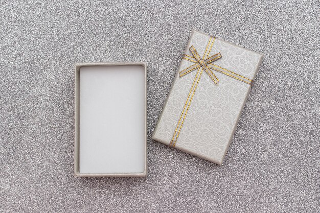 Раскройте серую подарочную коробку с смычком на серебряной сияющей предпосылке.