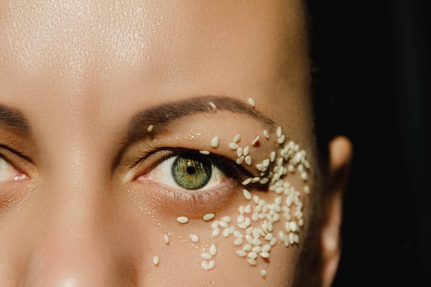 Open green eye of a woman with white sesame seeds on the eyelid around the eye Expressive look