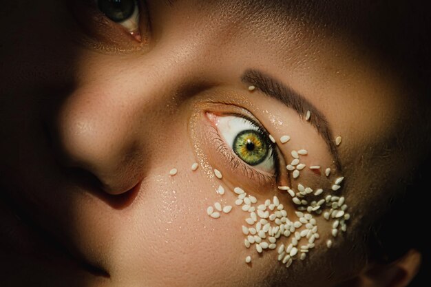 Open green eye of a woman with white sesame seeds on the eyelid around the eye Expressive look