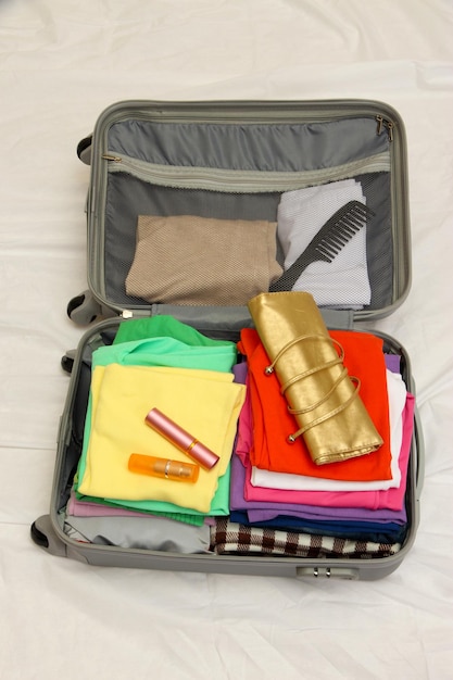 Open grey suitcase with clothing on bed