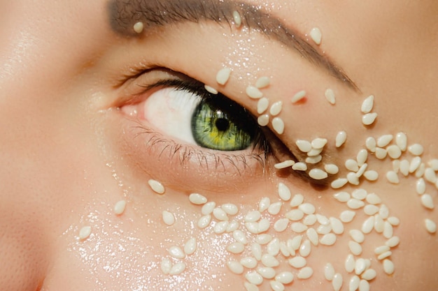 Open groen oog van een vrouw met witte sesamzaadjes op het ooglid rond het oog Expressieve look