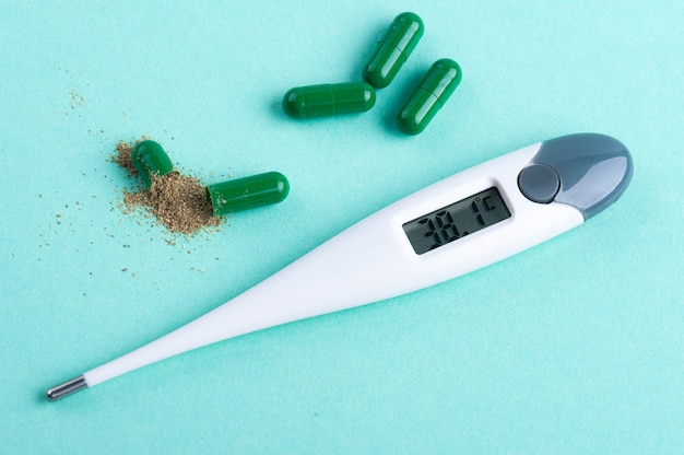 Open groene capsulepil met kruiden en thermometer op groen