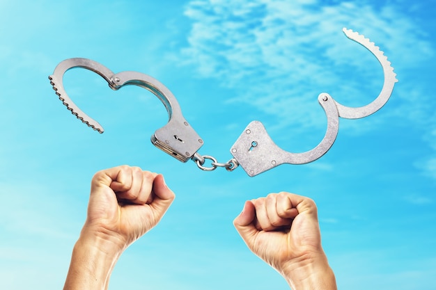 Open handcuffs and hands raised up amid the blue sky