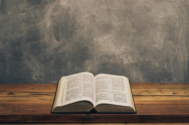 Open Holy Bible on a old oak wooden table Grey wall background