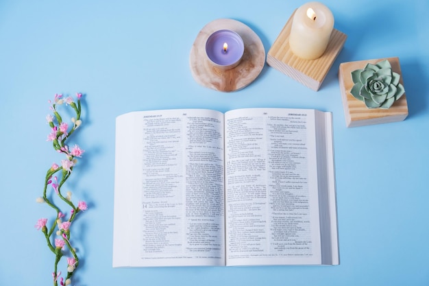 Open Holy Bible with sandles and decorative flowers on blue background