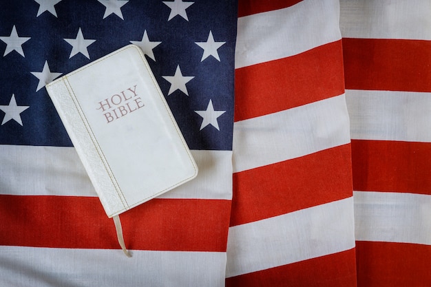 Open is het lezen van Heilig Bijbelboek met gebed voor Amerika over ruches Amerikaanse vlag in houten tafel