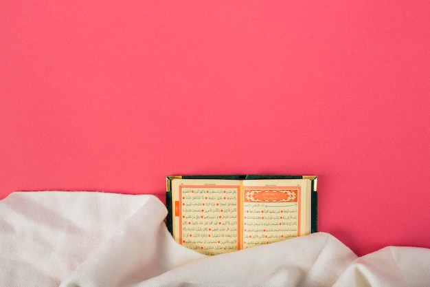 An open islamic holy kuran with white cloth against red background