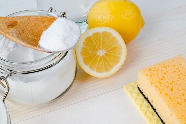 Open jar of baking soda with a wooden spoon on top vinegar cut lemon top view space for text