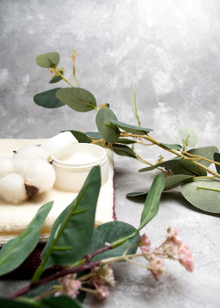 An open jar of cream is surrounded by eucalyptus branches Skin healing concept