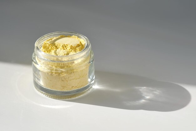 Photo an open jar of a yellow turmeric facial scrub showing off its texture