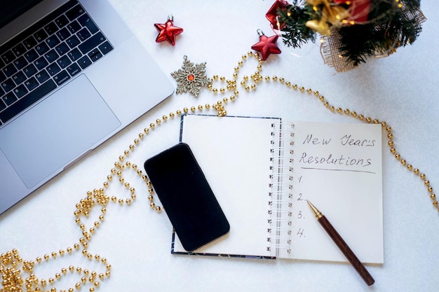 open kladblok met tekst nieuwjaarsresoluties en lege lijst decoraties laptop en smartphone