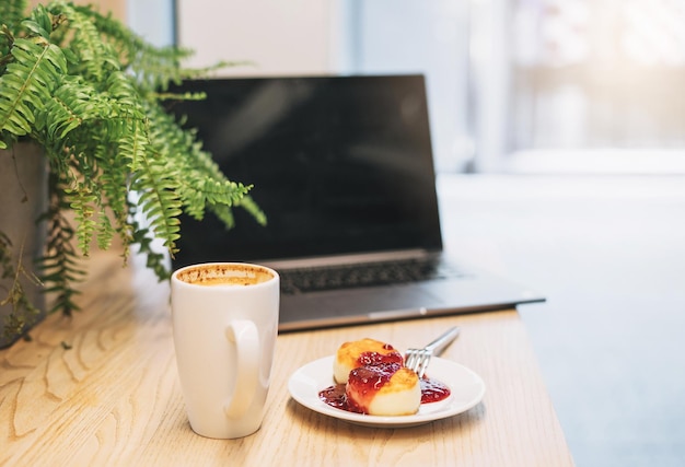 Open laptop cheesecakes met jam kopje cappuccino op tafel in café