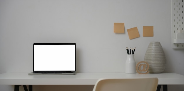 Open laptop computer in minimal workplace with ceramic vase and office supplies 