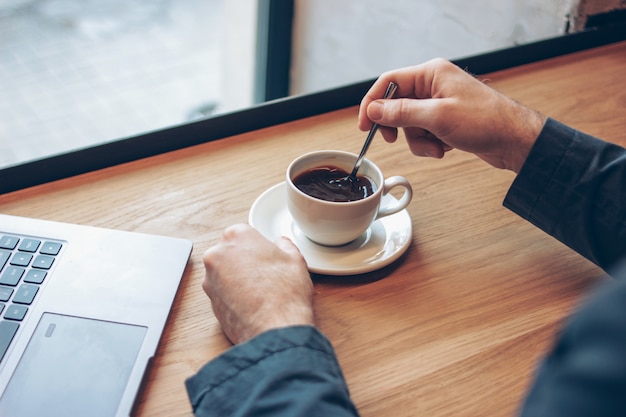 Open laptop en mannen handen met een kopje koffie op tafel in het café